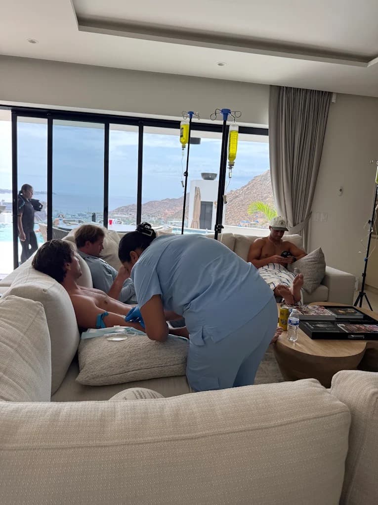 Nurse starting an IV for a guest on a sofa in a villa living room with ocean views