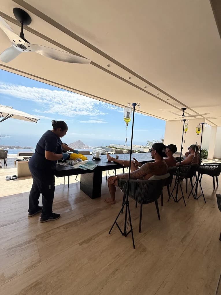 Nurse preparing IV supplies while guests relax on a villa terrace overlooking the bay